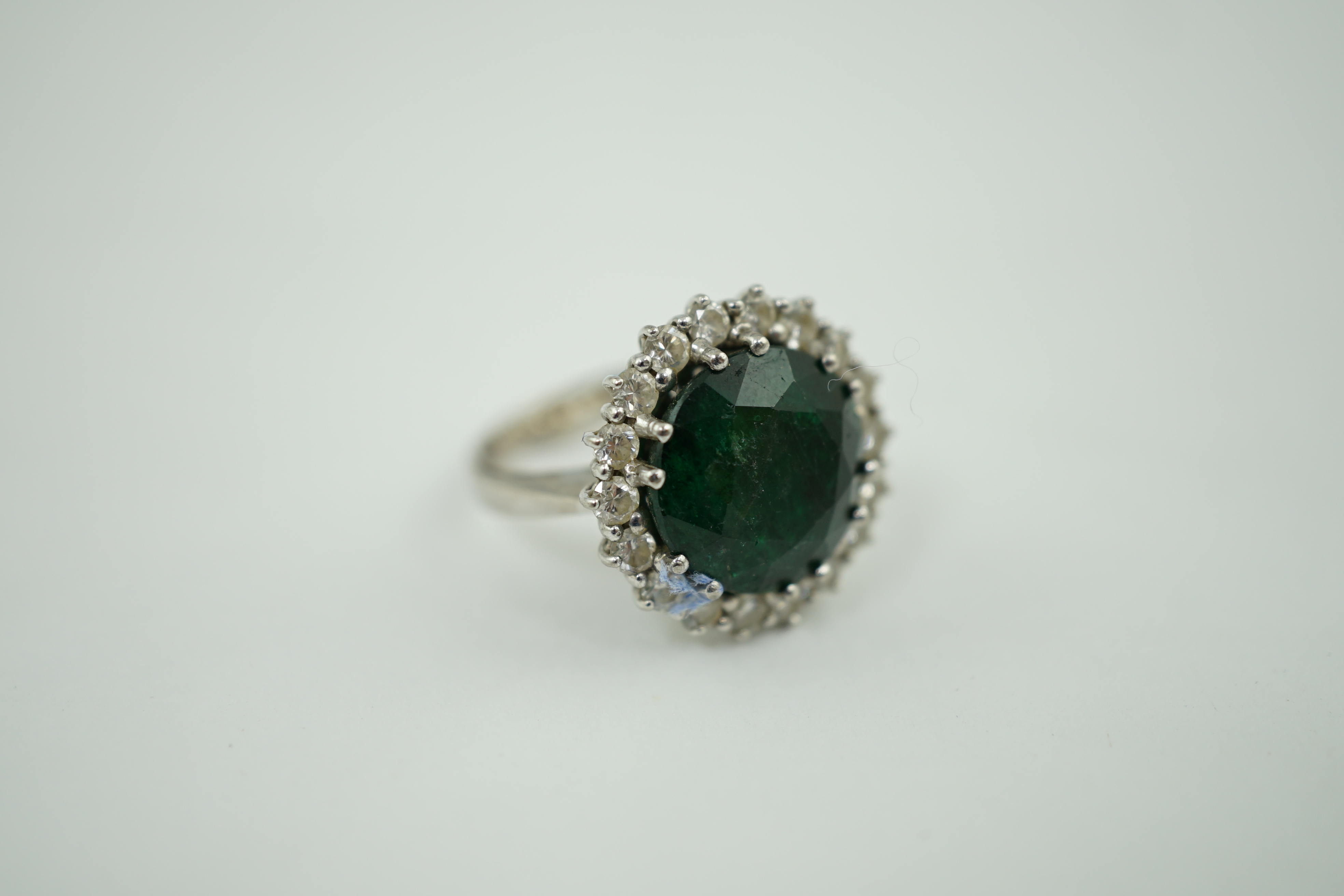 A mid 20th century 18k white gold and round cut emerald set dress ring, with diamond set border